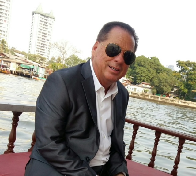 A man in suit and sunglasses sitting on the deck of a boat.